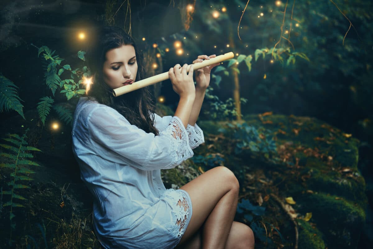 Beautiful forest nymph playing flute with fairies