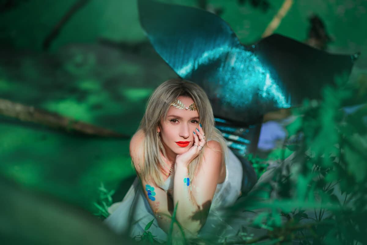 A beautiful girl in a transparent white cloth sits on a branch in a swamp. A mermaid with a diadem sits on a tree by a green reservoir. fantasy image