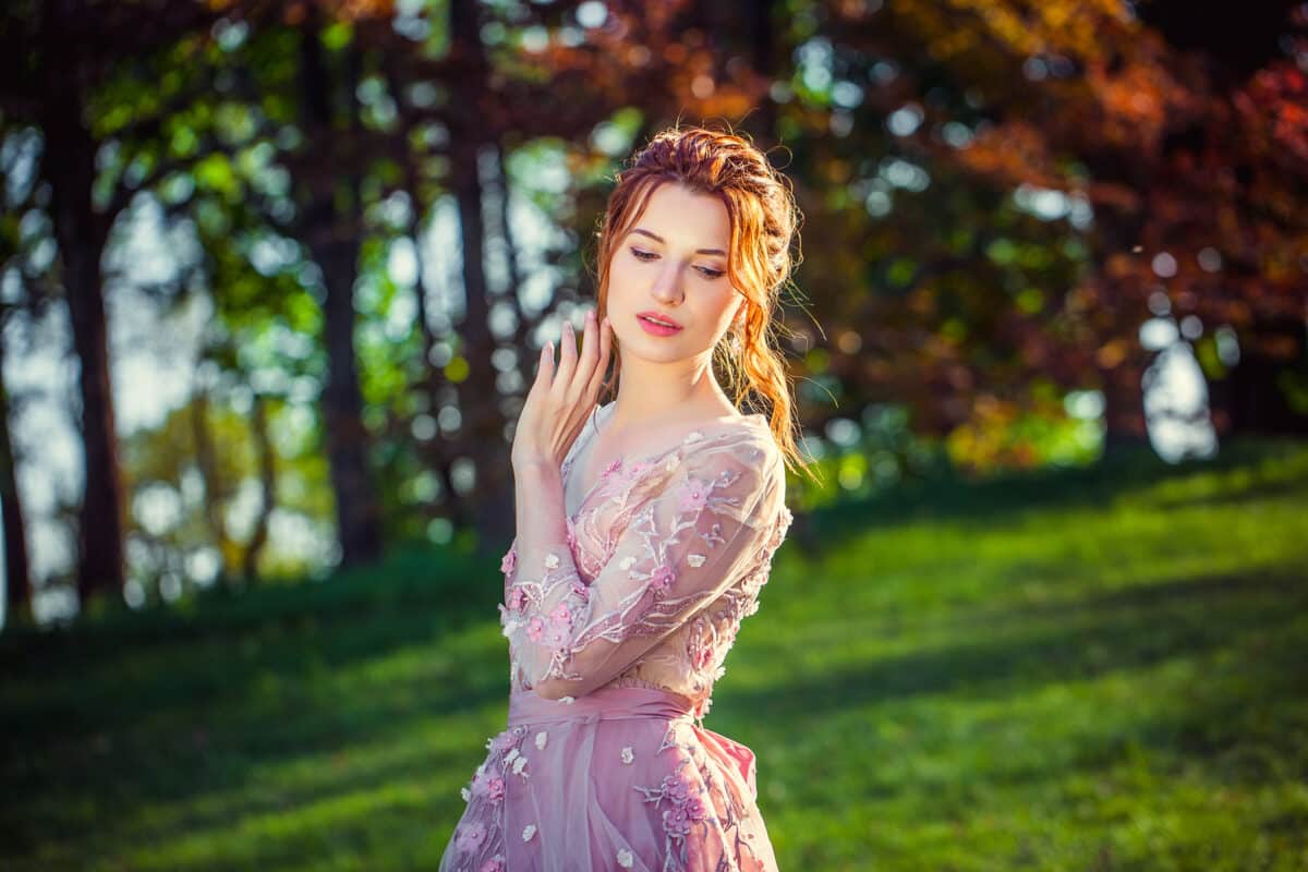 Beautiful girl with red hair in a pink dress. background of a green park