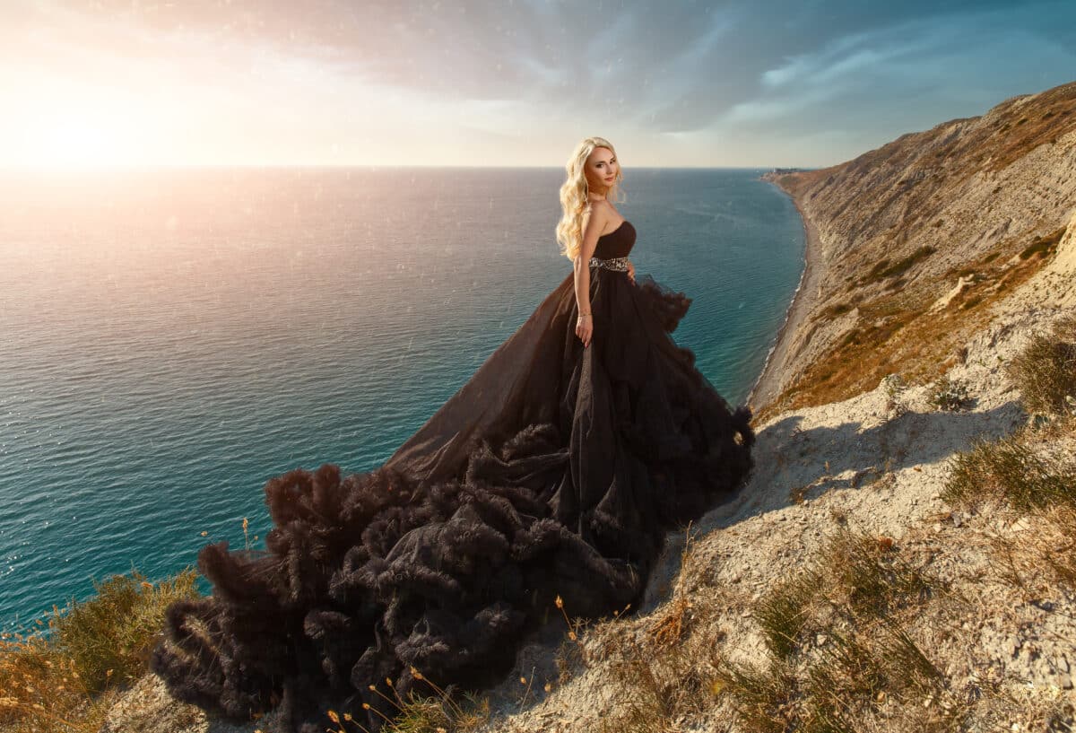 beautiful blonde girl in a black long dress on a mountain cliff overlooking the sea.