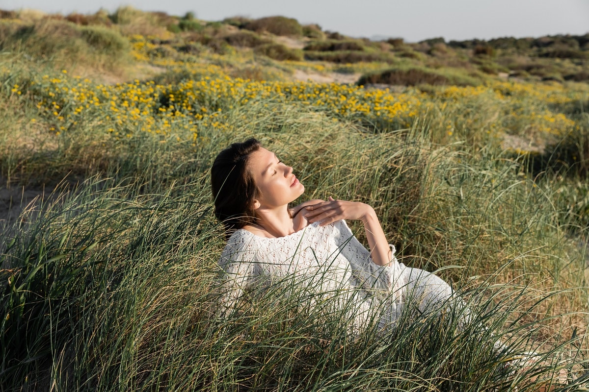 Woman in summer dress relaxing on grass on beach with wildflowers