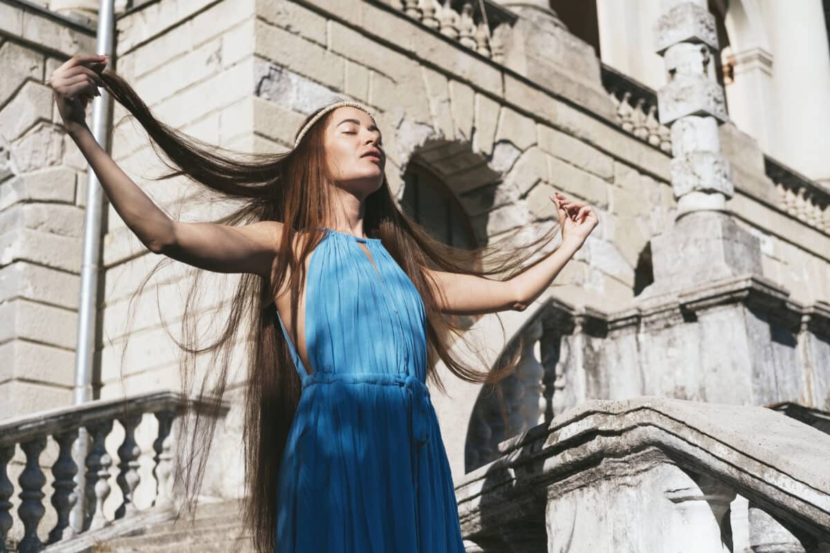 Beautiful lady dressed in blue with very long hair standing near an ancient palace