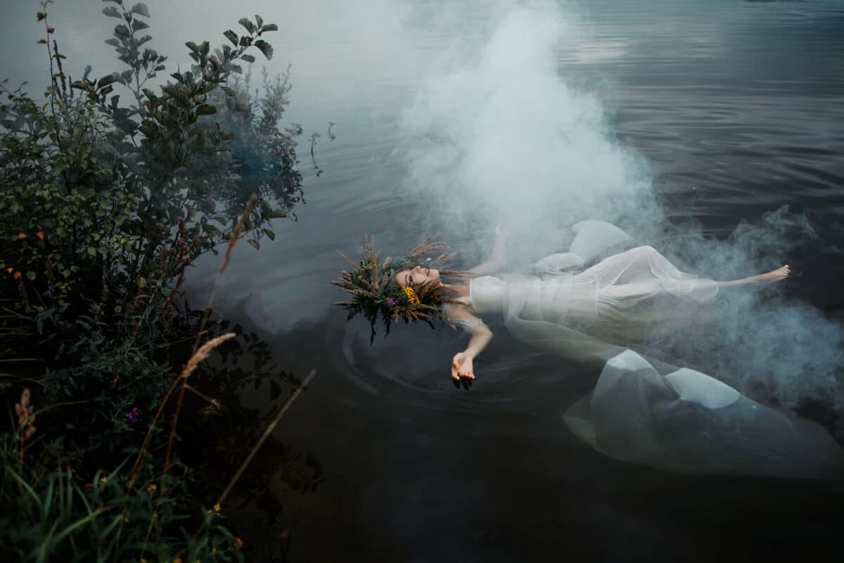 A lake nymph in a white dress and a wreath of flowers floats on the surface of the water. A young woman in a folk image, a mystical story