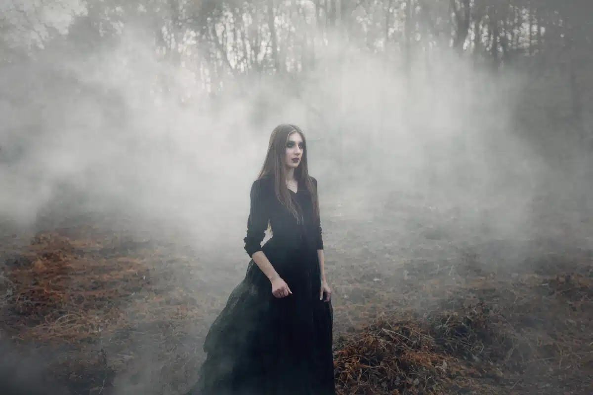 Young attractive Witch walking on the field in heavy black smoke.