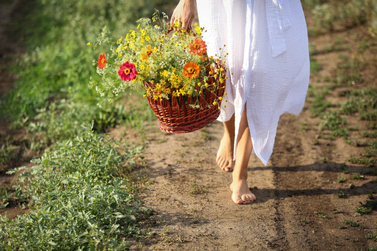 barefoot lady carries a wooden basket with wild flowers