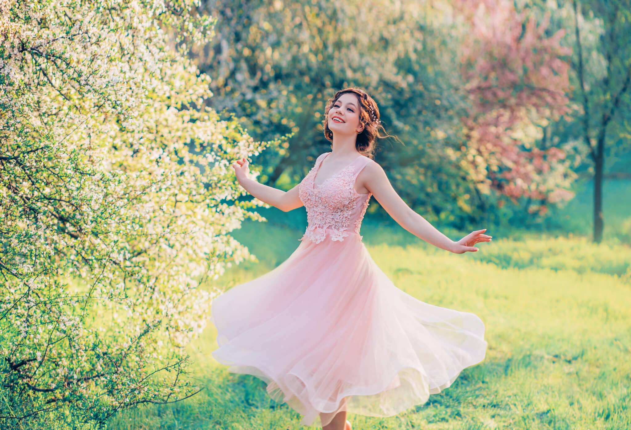 happy girl in short flying gentle pink dress laughs joyfully, doll princess whirls in bright yellow spring garden with flowering trees, positive emotions, movement in photo with creative colors.