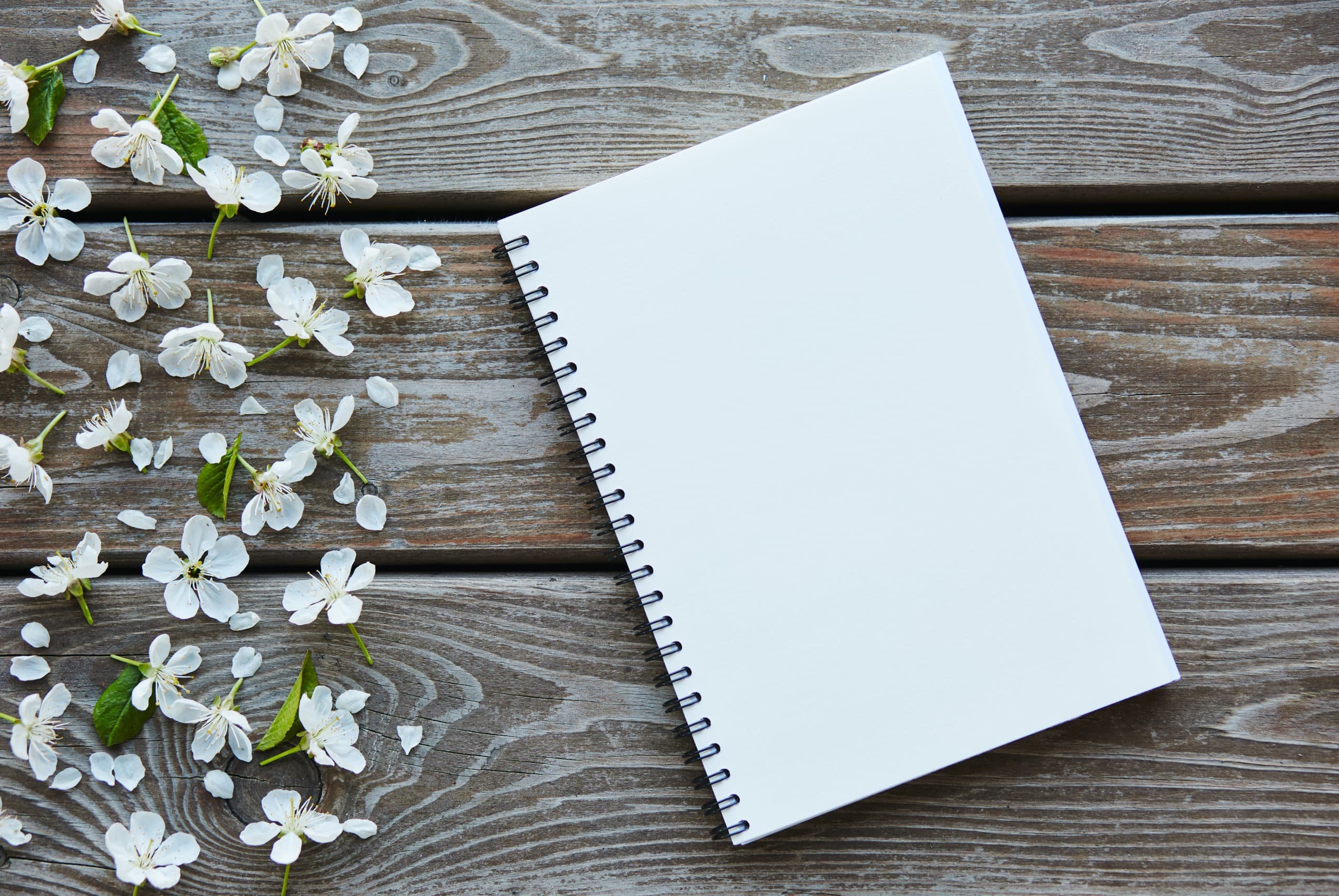 An empty notebook covered with cherry flowers on a wooden table.