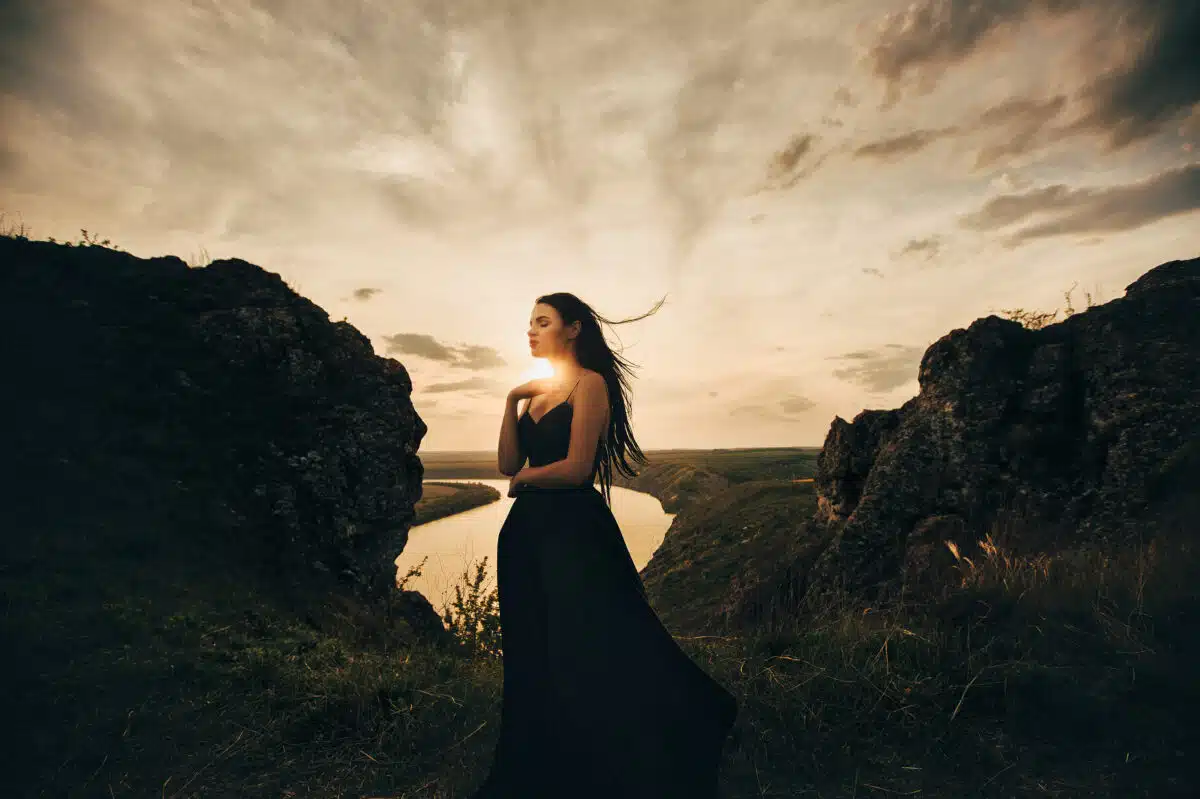 woman in a long black dress standing on a mountain top in the evening