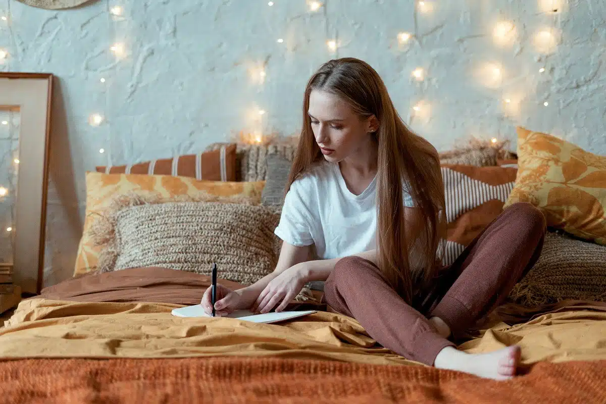 Young lady looking relaxed in her bedroom, writing in her notebook.