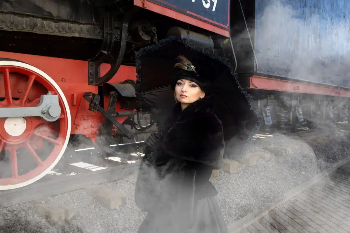 a beautiful lady in a historical retro dress against the background of an old steam locomotive at a railway station