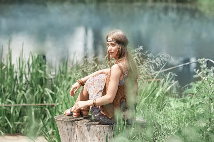 beautiful hippie girl sitting on a stump and looking at the pond