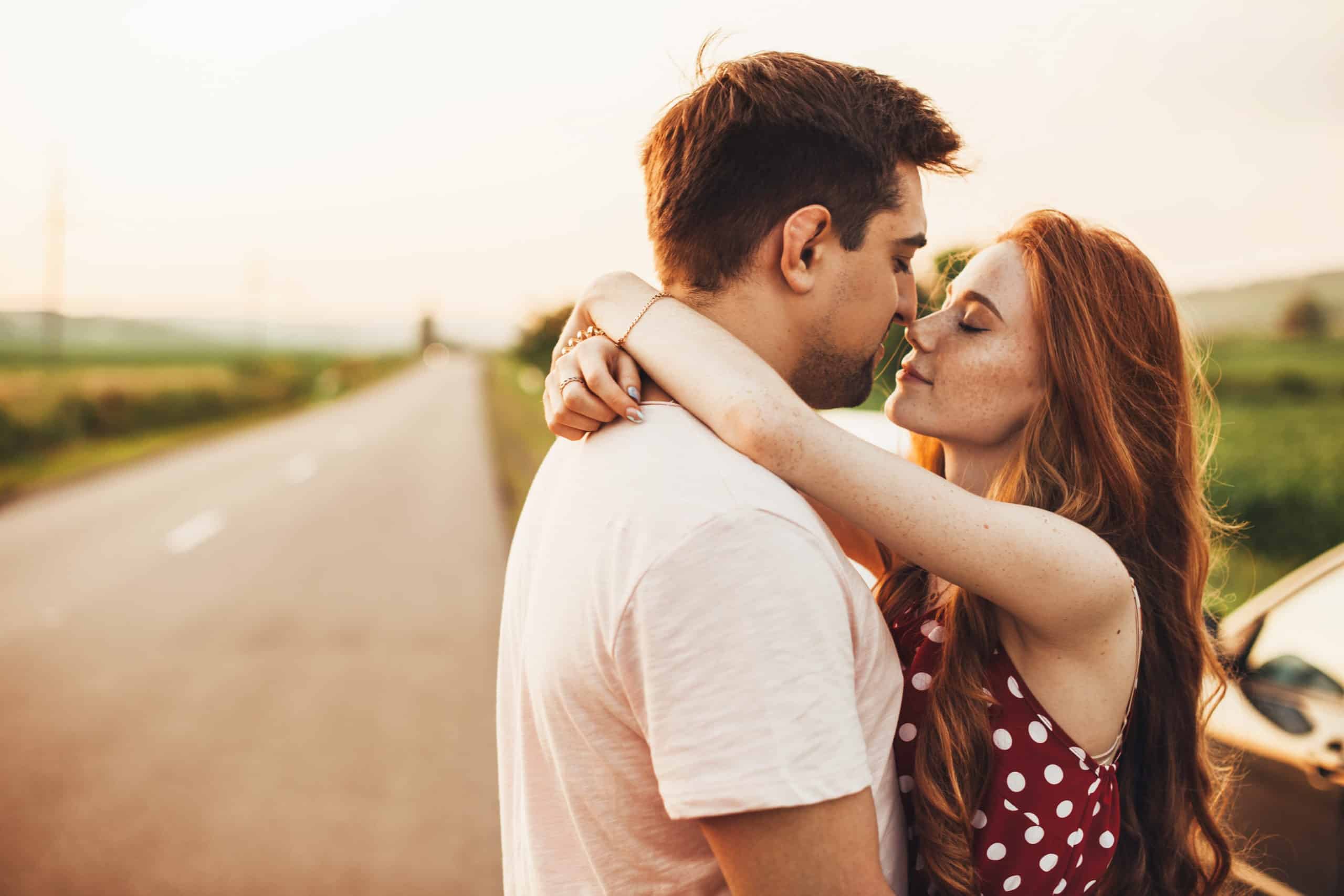 A red-haired girl in love embracing her boyfriend enjoying the moment with her eyes closed while standing on the side of the road.