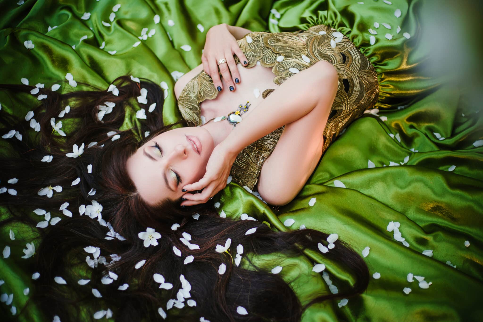 A beautiful young woman in a green dress lies on a train among the white petals of an apple tree.