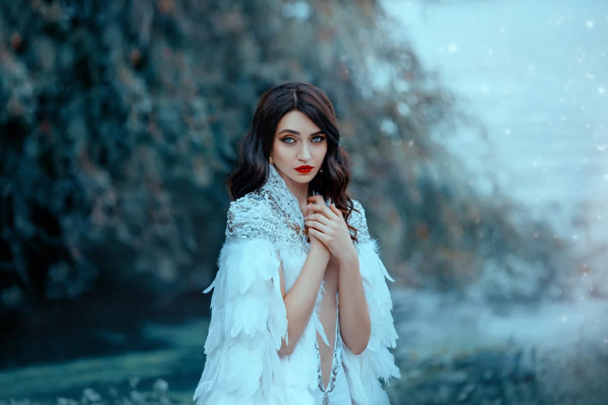 Attractive pretty woman in a white cape with silver and feathers. The gentle snow queen. Portrait of a luxurious brunette, hairstyle retro style cold wave. Big blue eyes and red lips.