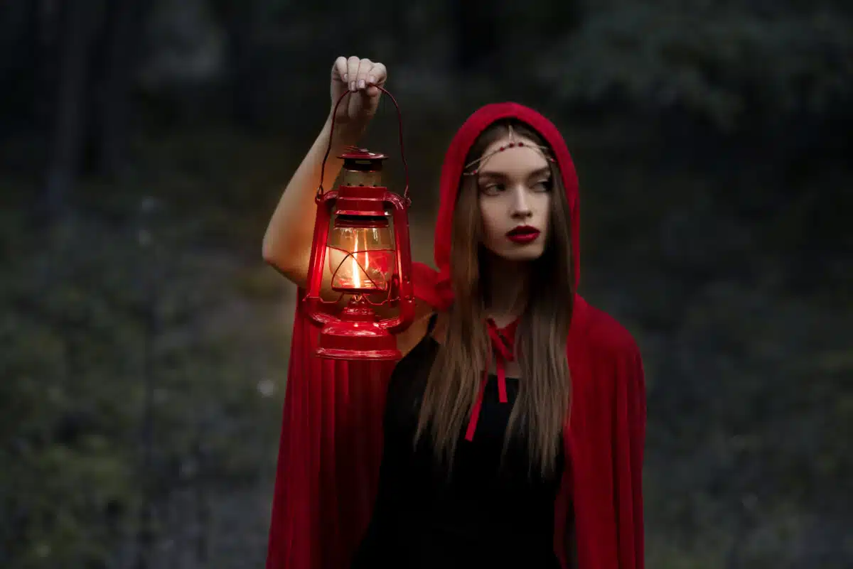 elegant mystic girl walking in dark forest with kerosene lamp
