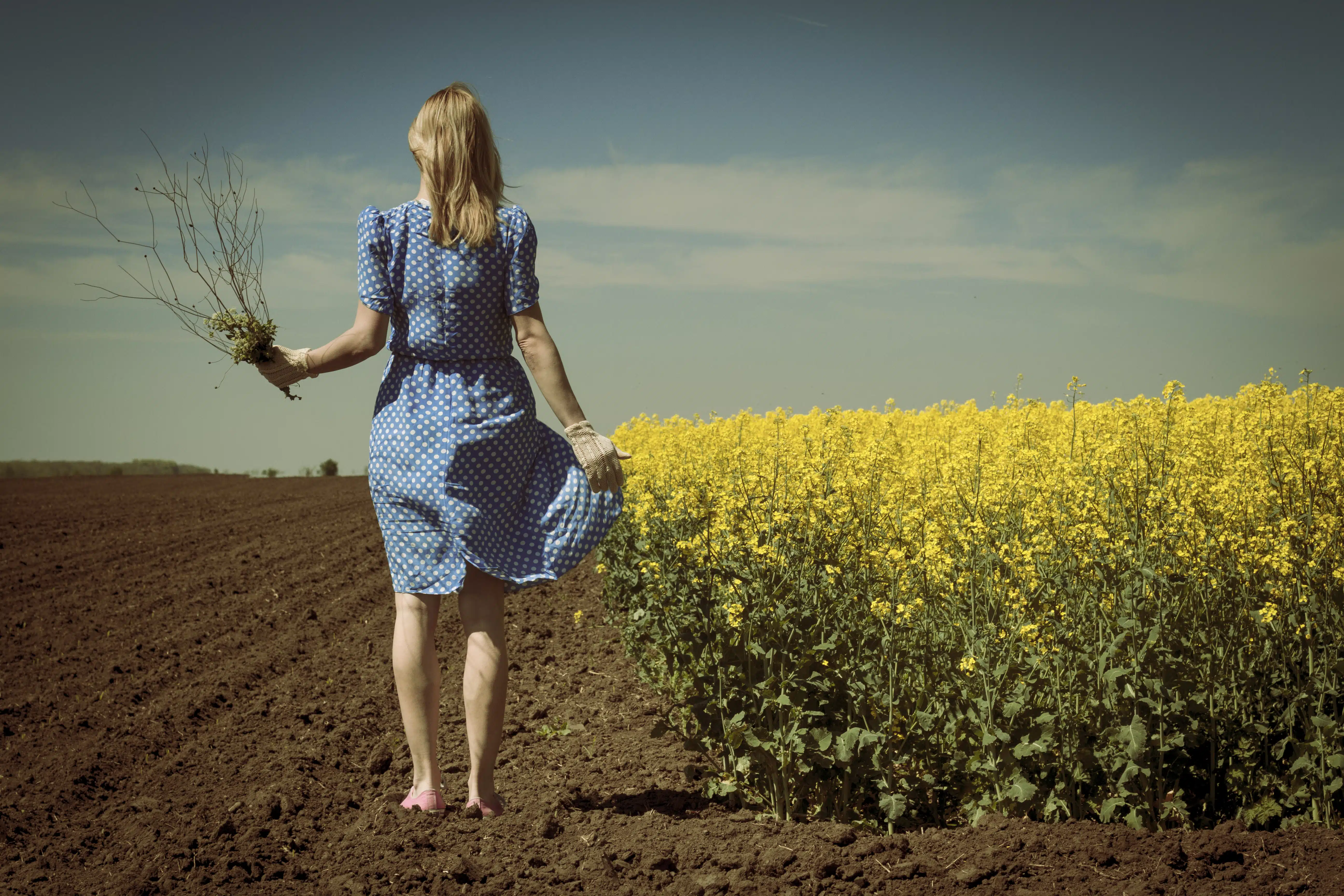 lonely woman in canola field holding flowers