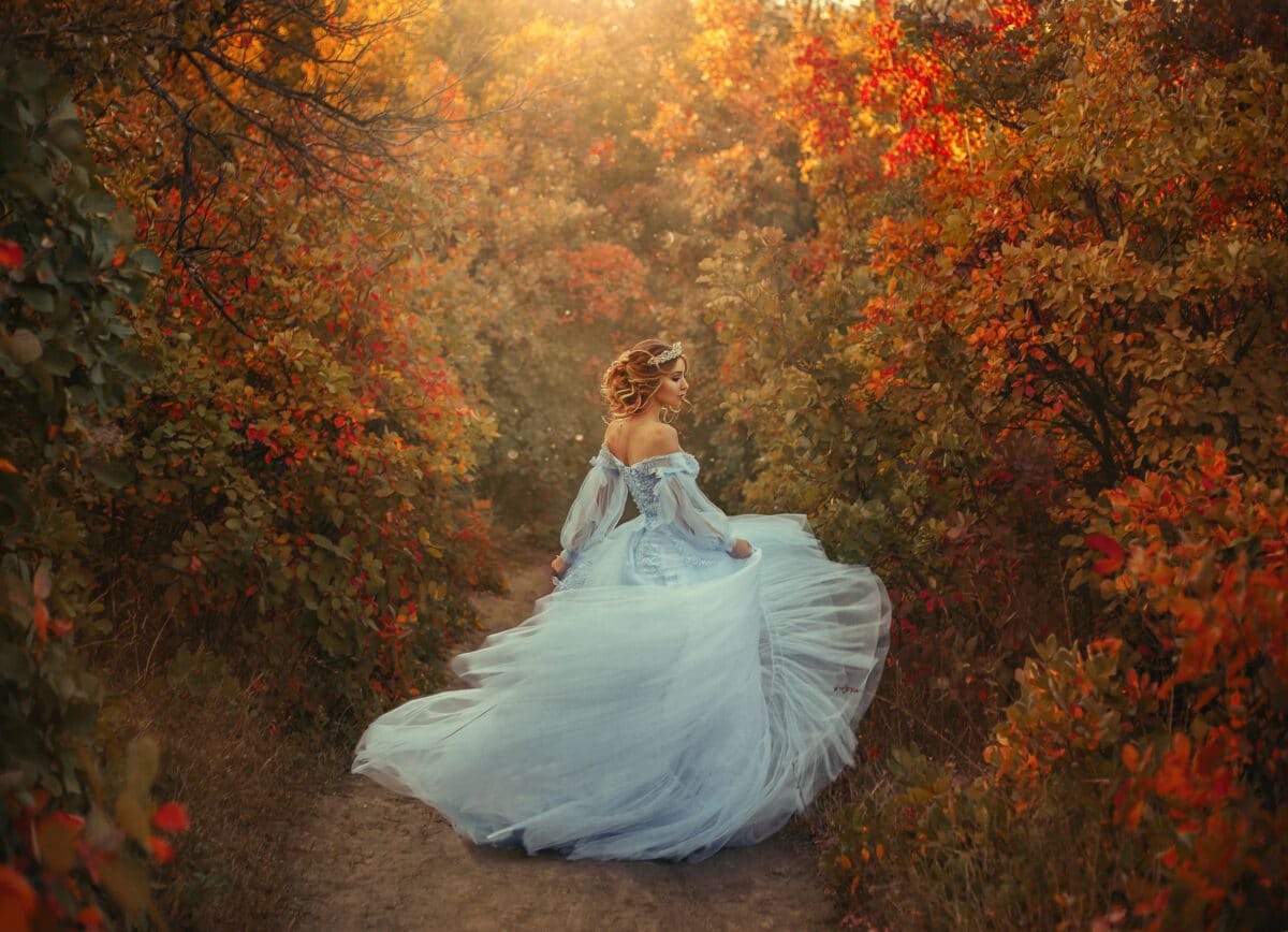 A young princess turns in a beautiful blue dress. The background is bright, golden autumn nature.