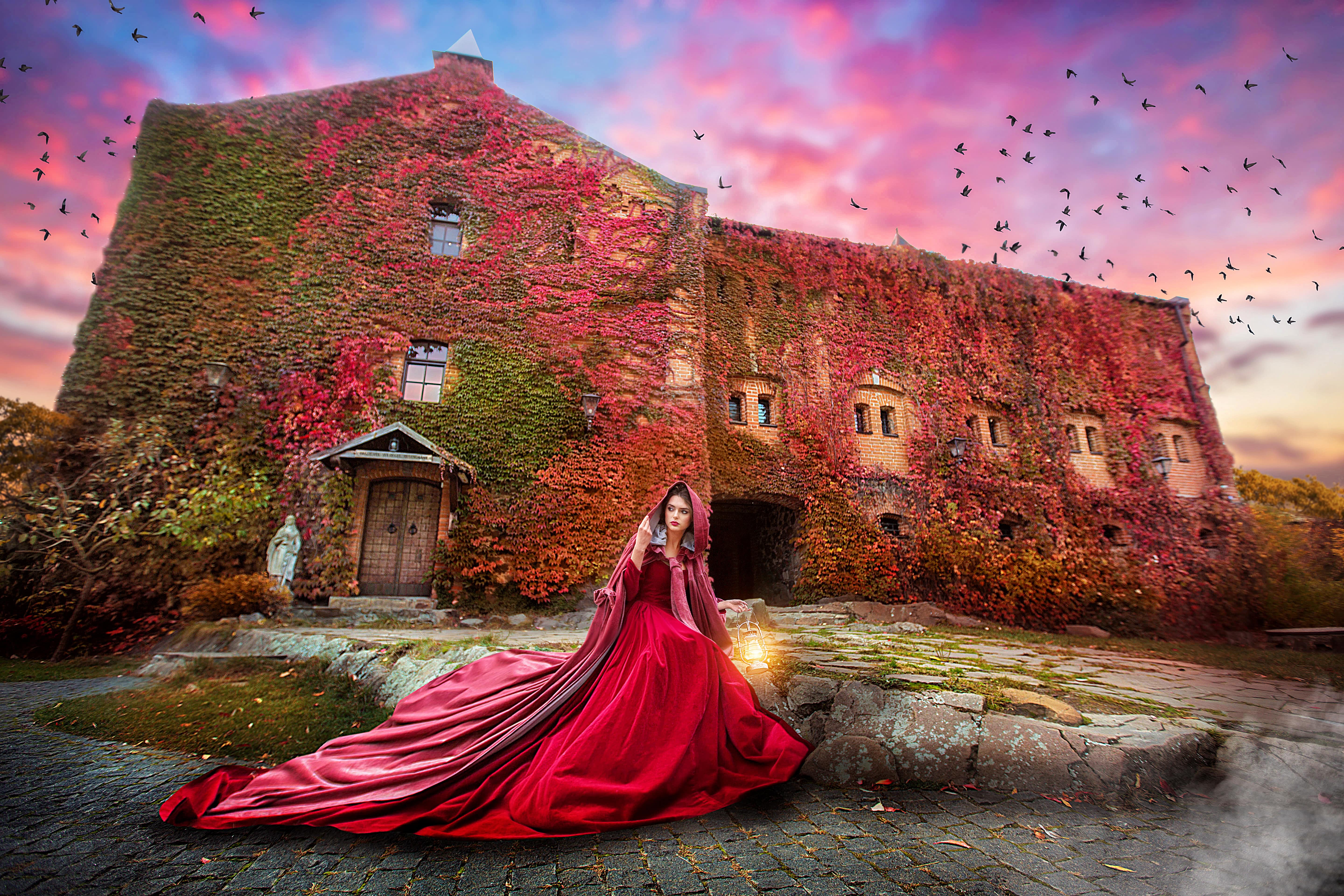 Beautiful lady in a burgundy coat and red dress sitting on the ground with a castle behind her