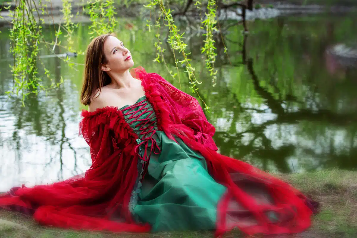 beautiful brunette young woman in red gown sitting by lake