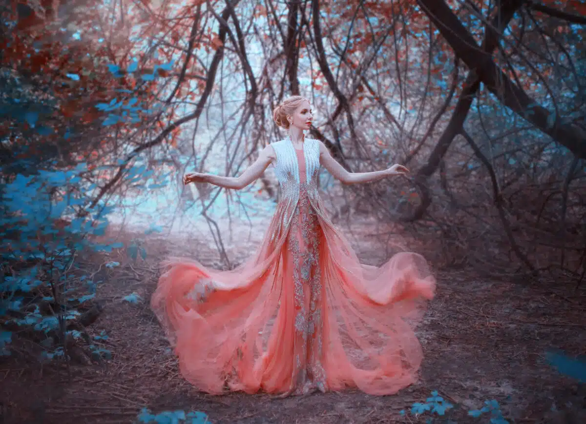 delightful queen standing in the forest near the branches of trees that touch the ground