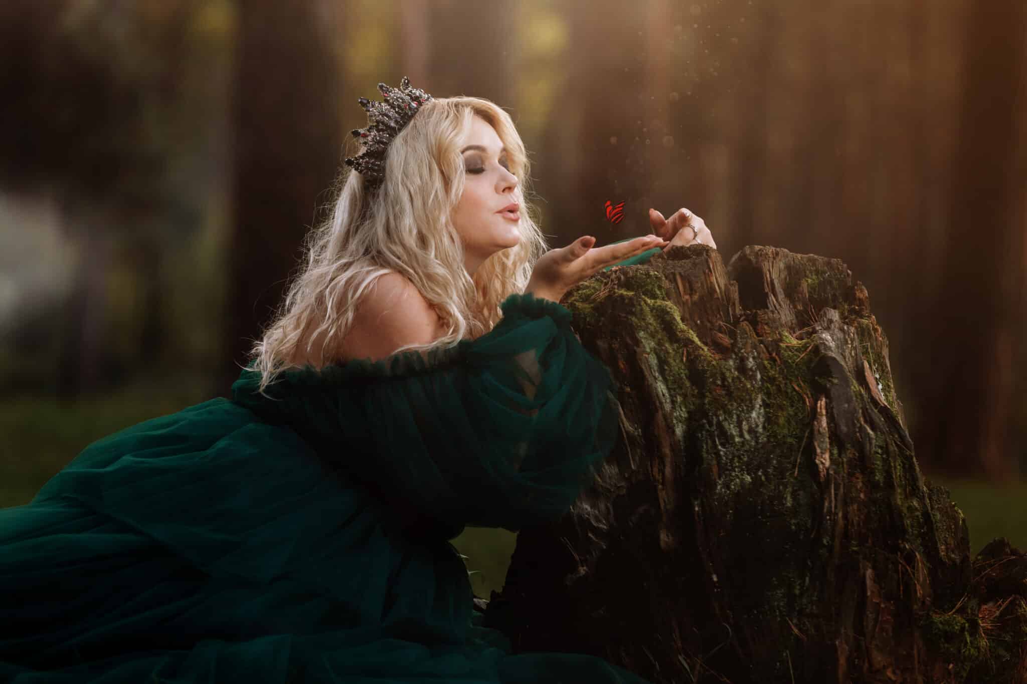 A beautiful blonde young woman in a long green dress and a diadem on her head in the forest. 