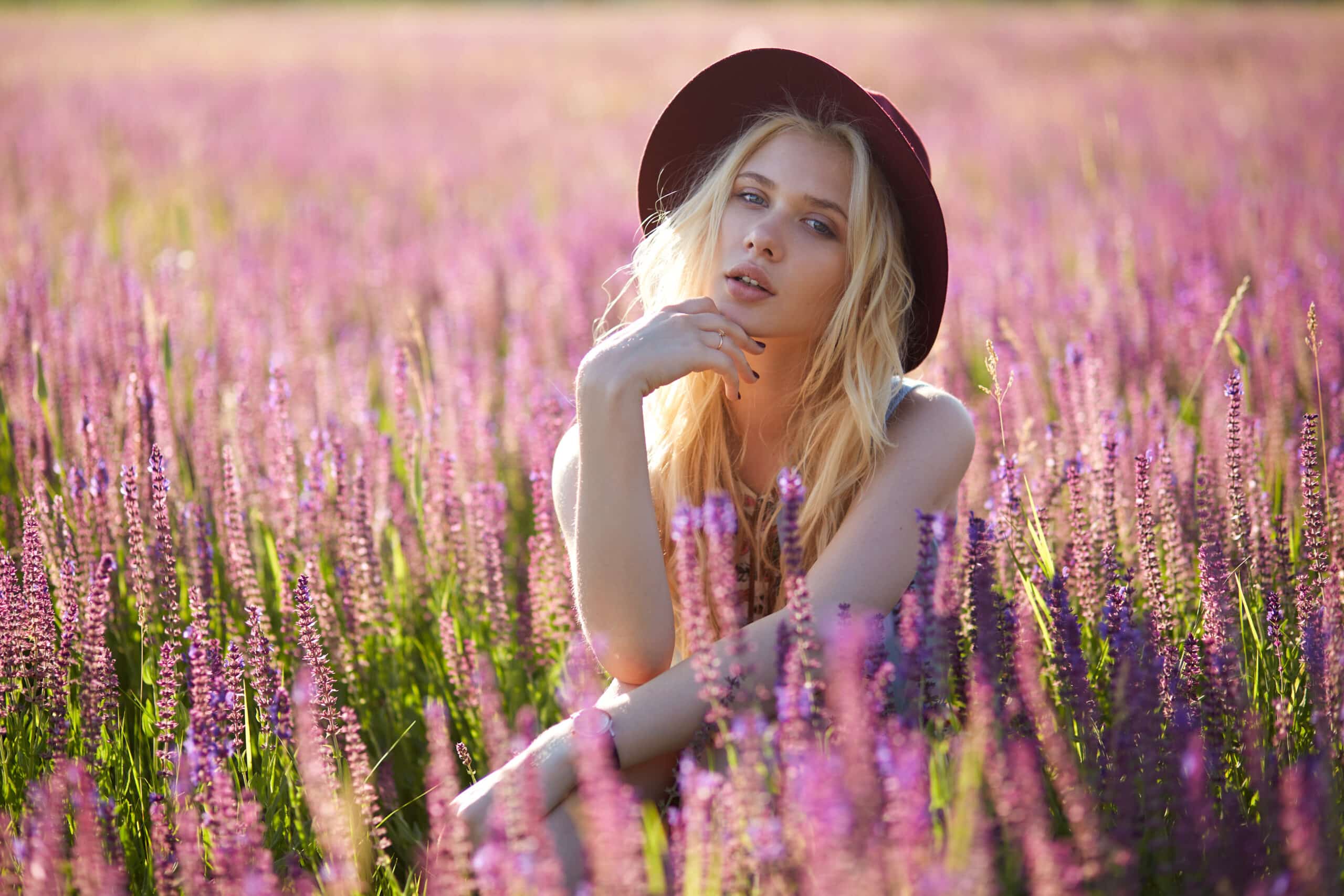 Cheerful blonde woman wears a hat in a floral field, behind beautiful sunset
