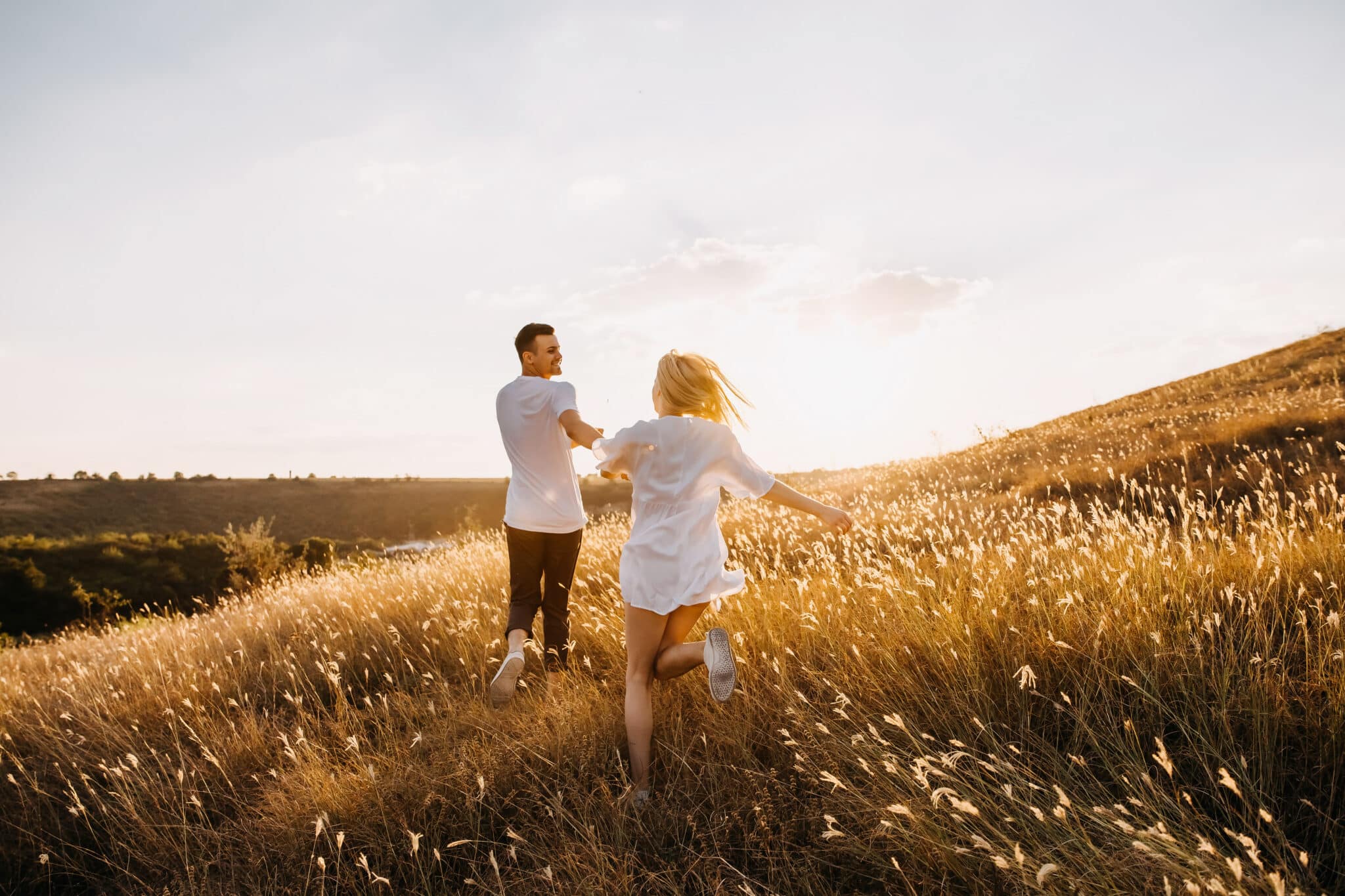 romantic couple running in an open field with dry grass at sunset