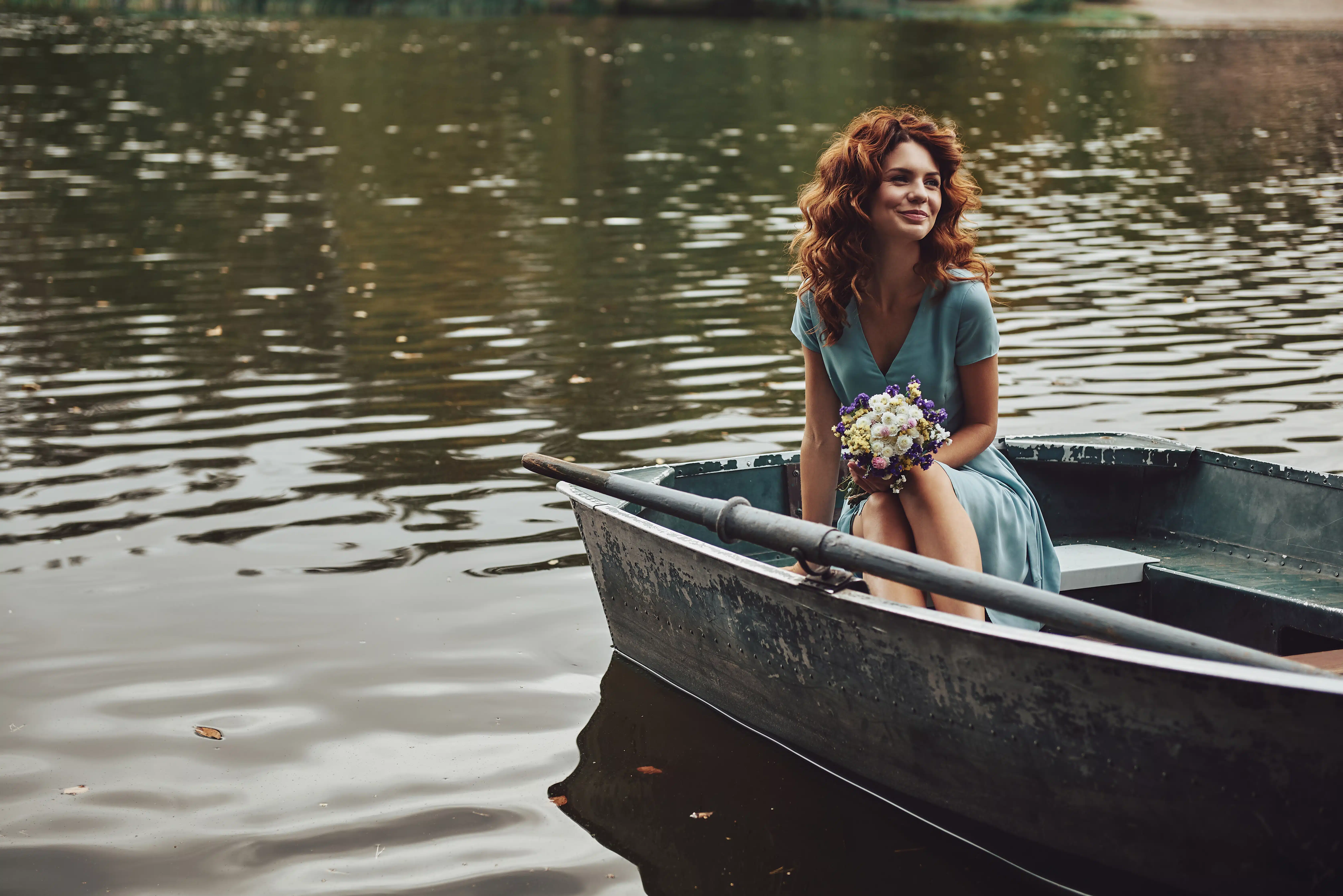 Charming young woman in elegant dress on a boat holding flowers