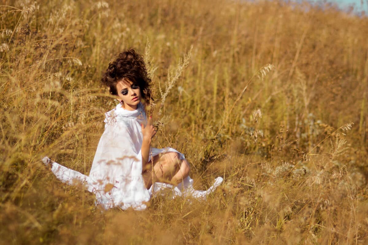Tender lady in a white dress sitting in the field of wild grass