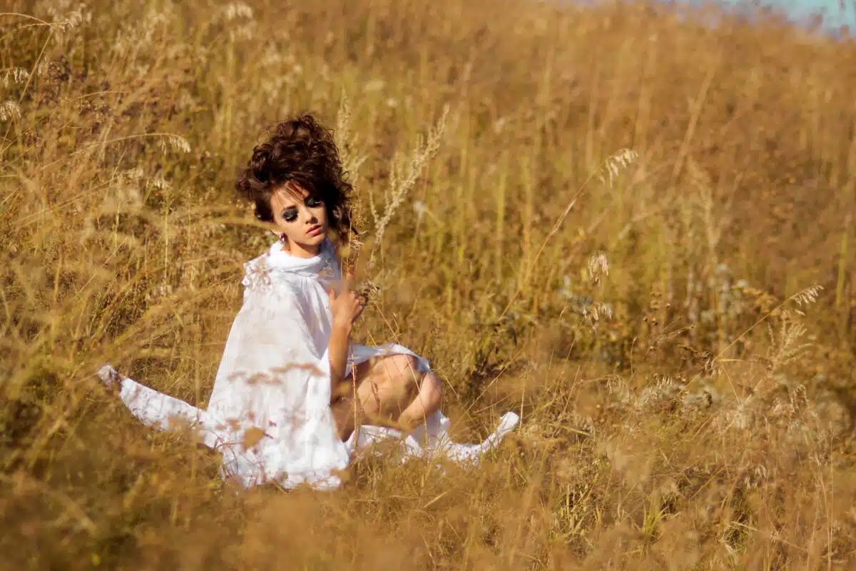 Tender lady in a white dress sitting in the field of wild grass