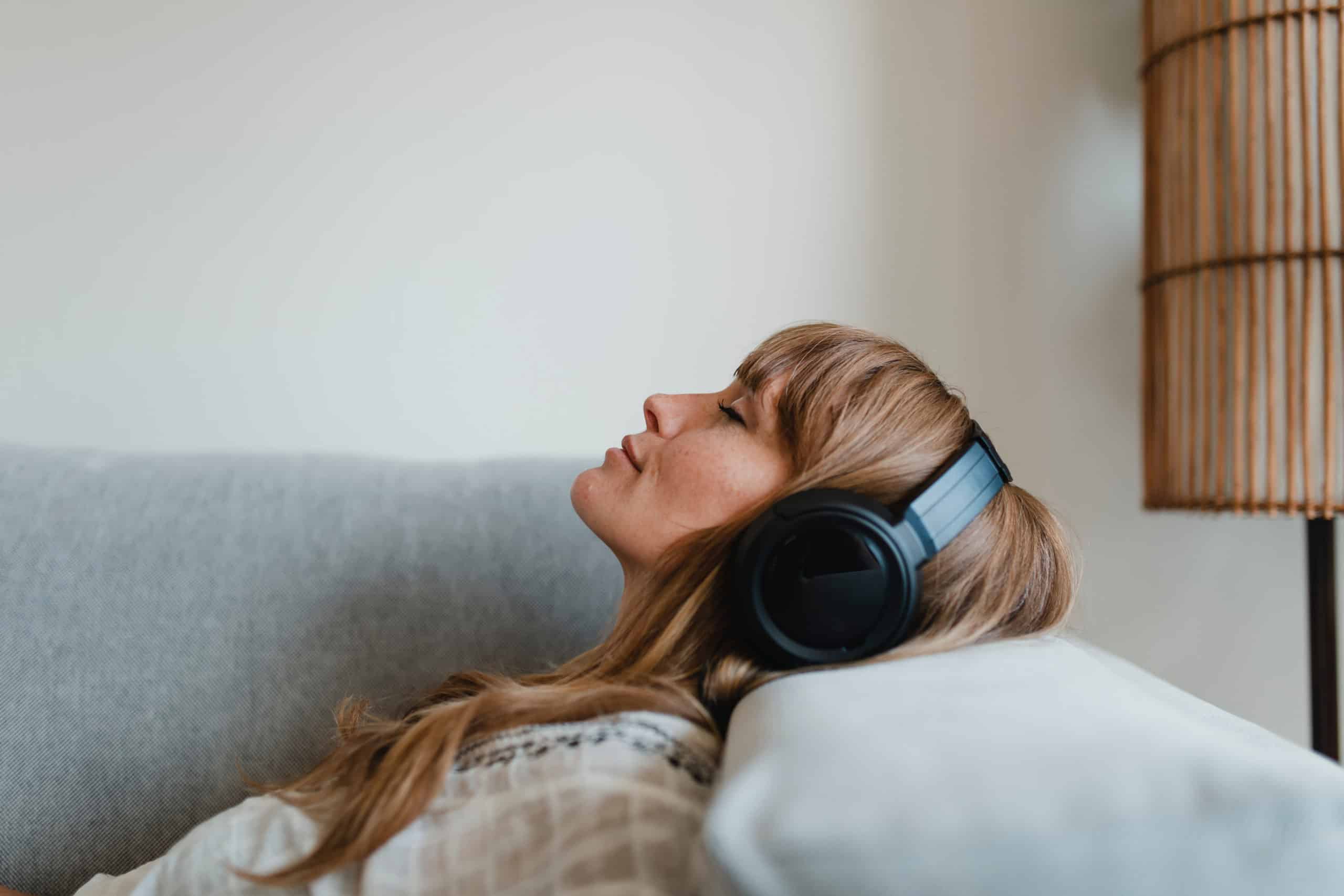 Woman relaxing on sofa, listening to music at home.