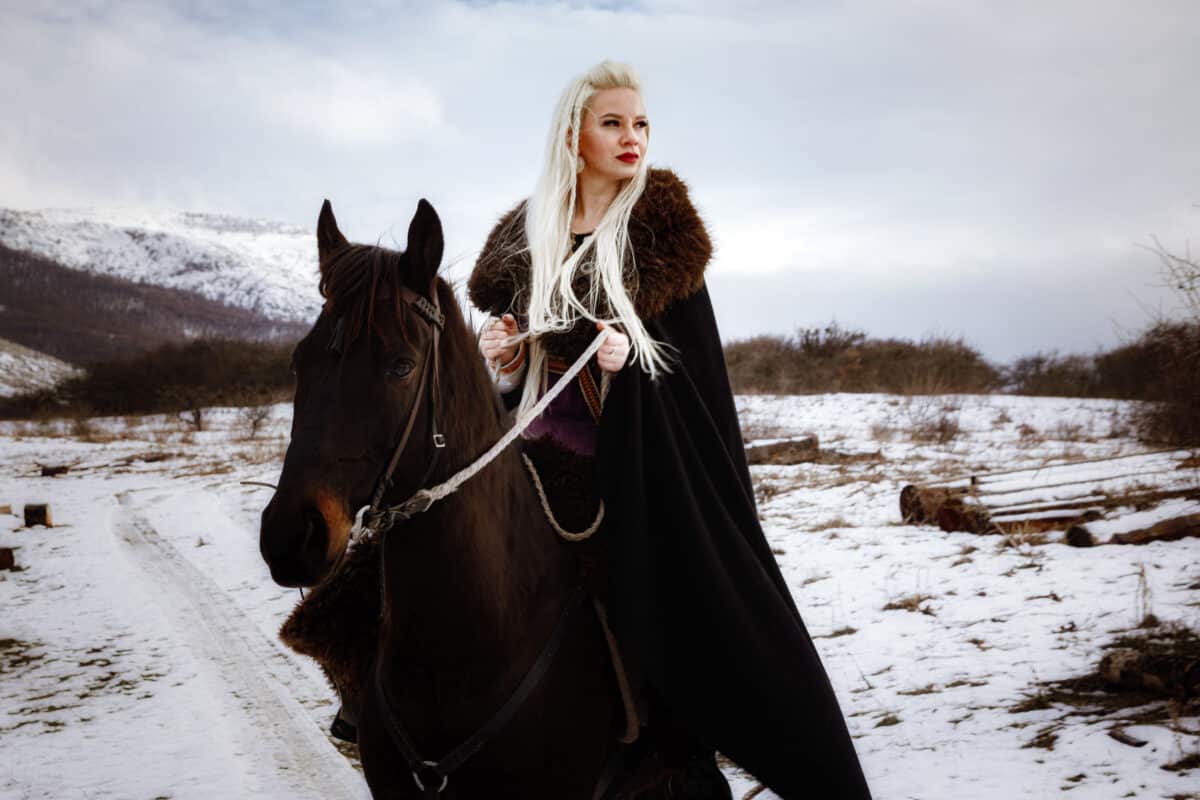 female viking with a black horse with view of the mountains in winter

