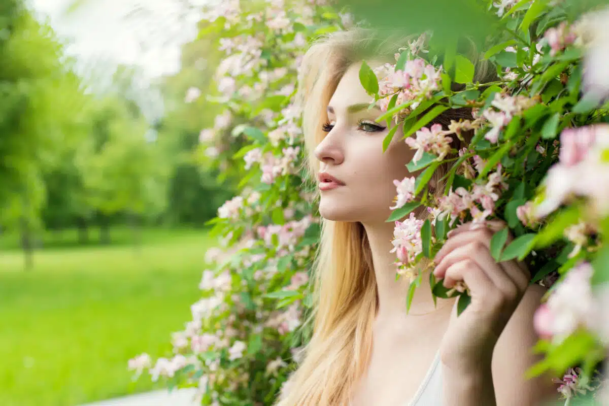 
enchanting young lady standing against the blooming bush