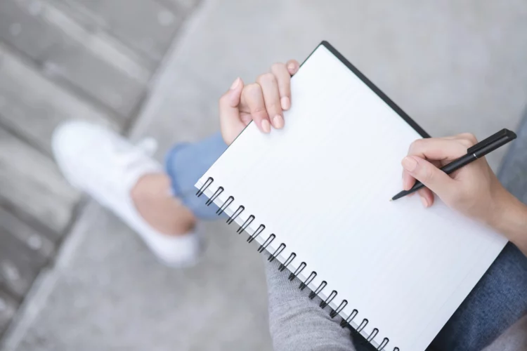 female hands with pen writing on notebook while sitting
