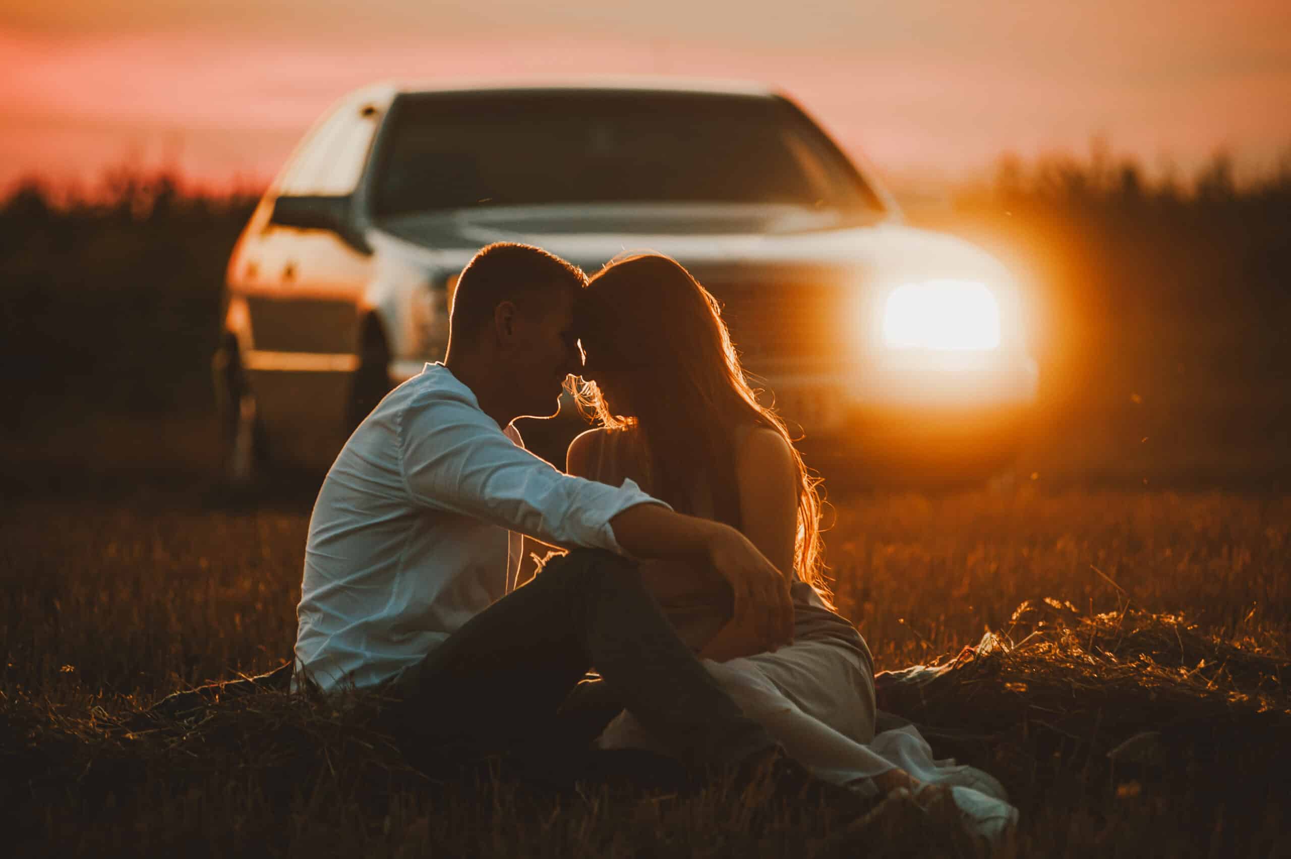 A beautiful photo of a couple siiting in field on sunset, on car