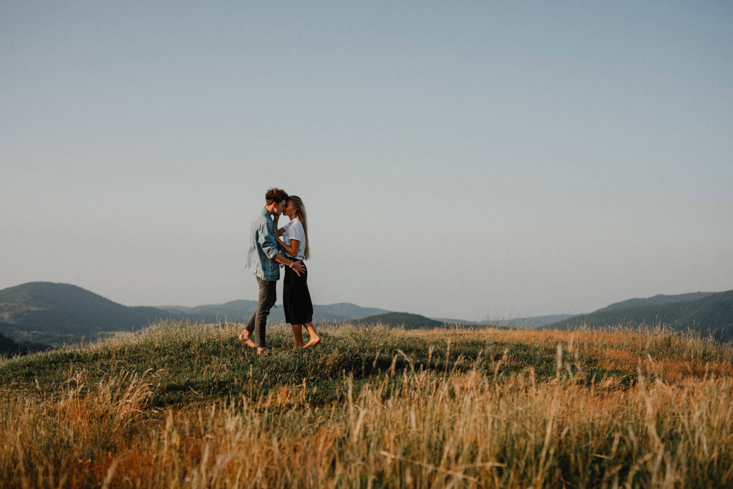 Young couple on a walk in nature at sunset in countryside, kissing.