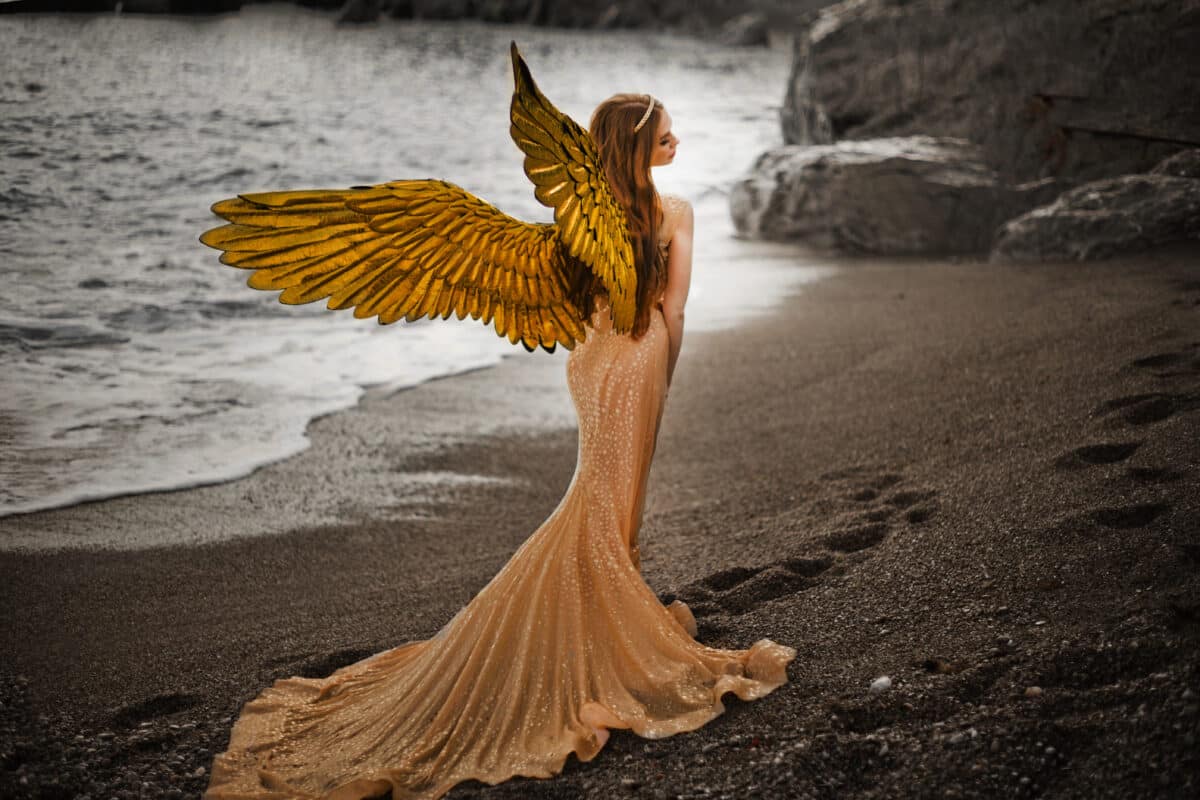 Young beautiful woman with bird wings standing on the beach