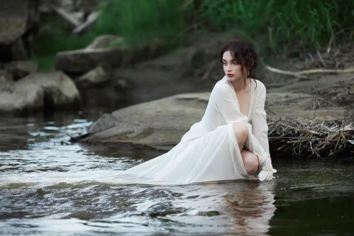 sensual young woman in a long white dress sitting in the river
