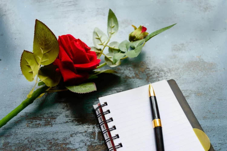 blank page note, pen and a beautiful red rose on rustic blue table.
