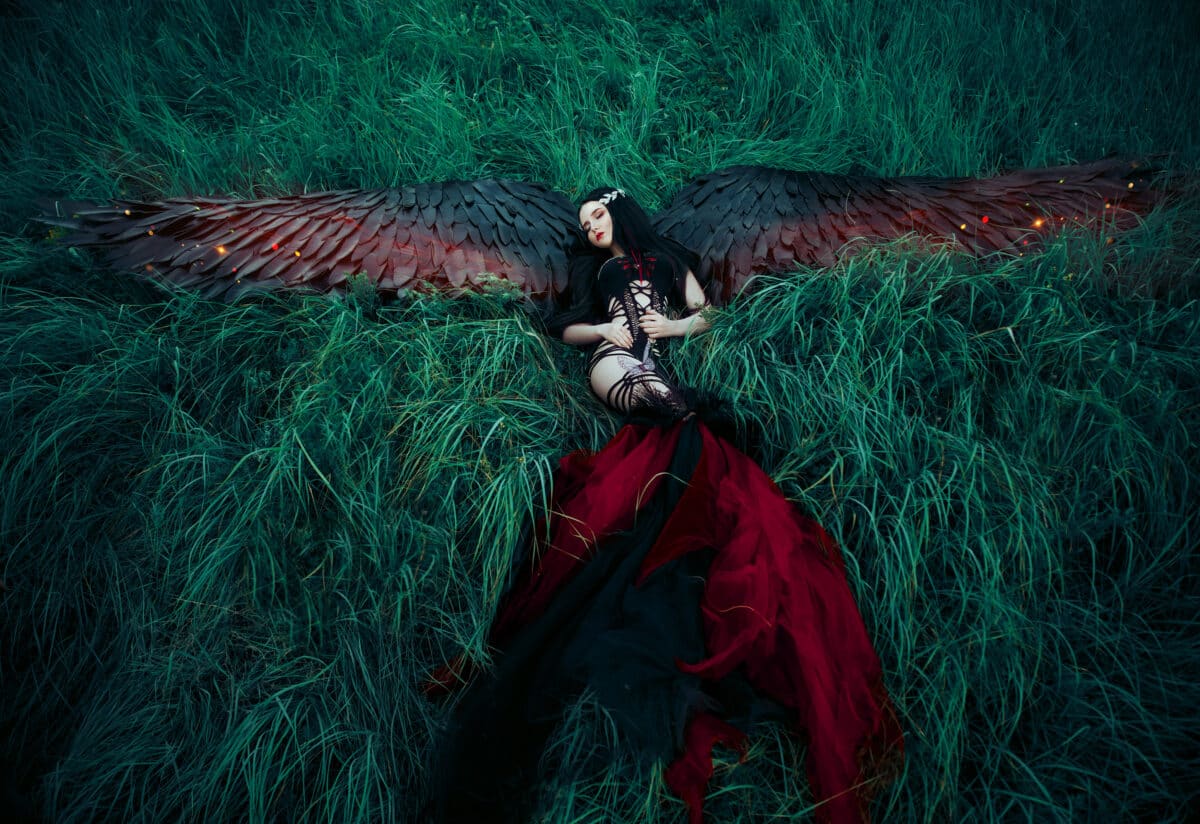 black fallen angel with a red plumage walking on the dark background of rocky mountains , vampire, hip toning, creative color, dark-Boho