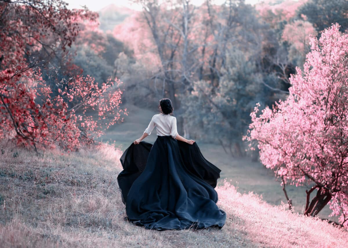 Princess in a vintage dress escapes. Walk through the picturesque autumn hills at sunset in pink tones. A long train of skirt fluttered on the run. Photo of a brunette girl with a back without a face.
