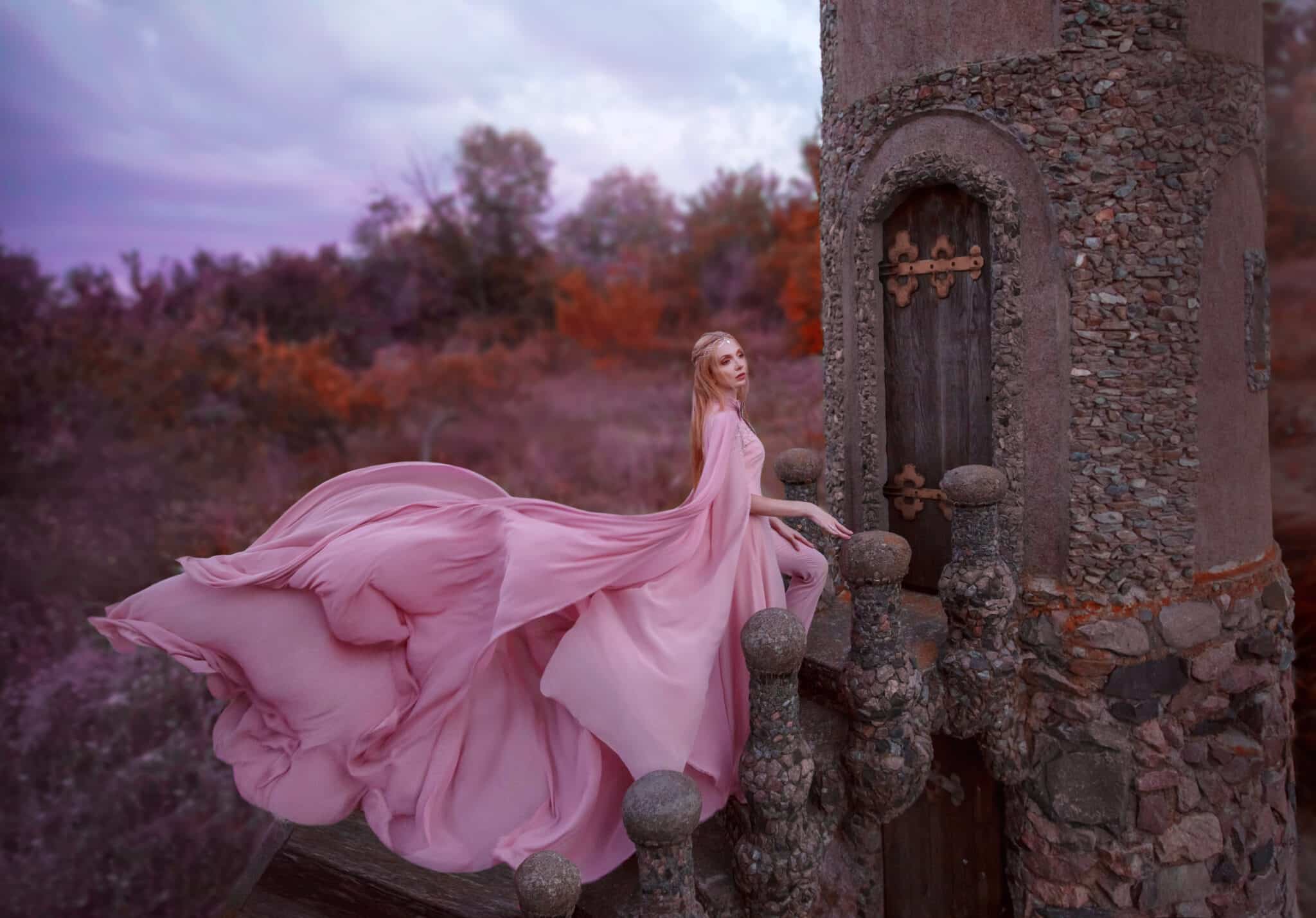 wonderful elegant girl elf with blond fair hair with tiara, wearing a luxurious long light pink fluttering dress standing on the castle staircase