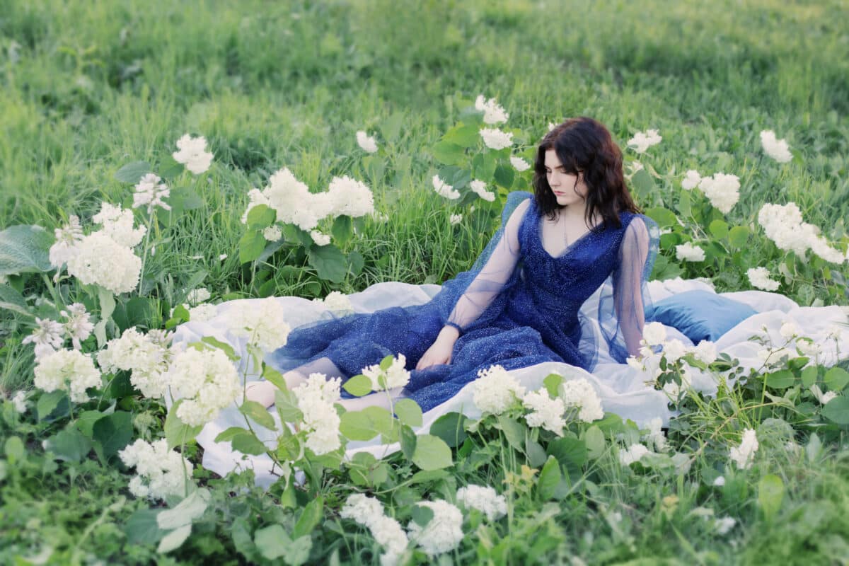 young beautiful woman in blue dress on grass with white flowers