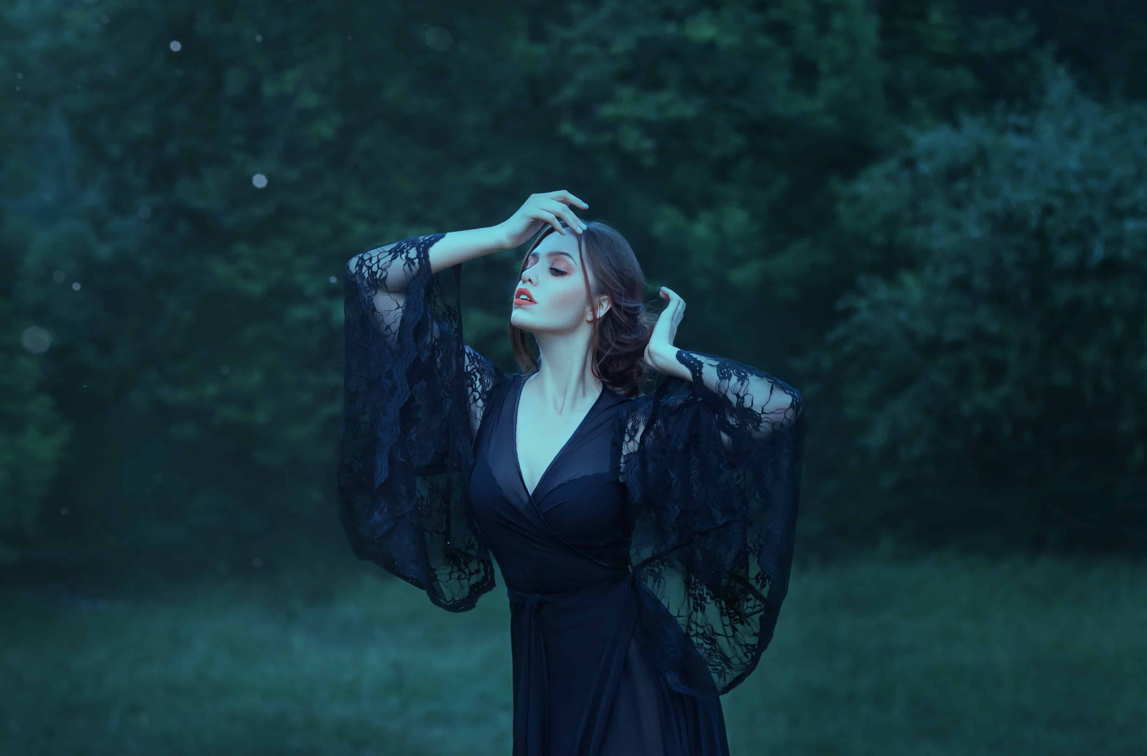 close eyes, girl dancing in the moon light in the dark emerald forest alone. magic. witch. demon. wearing a black long dress with lace sleeves.