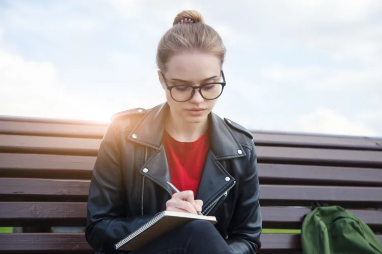 thoughtful young woman wearing eyeglasses writing notes outdoor