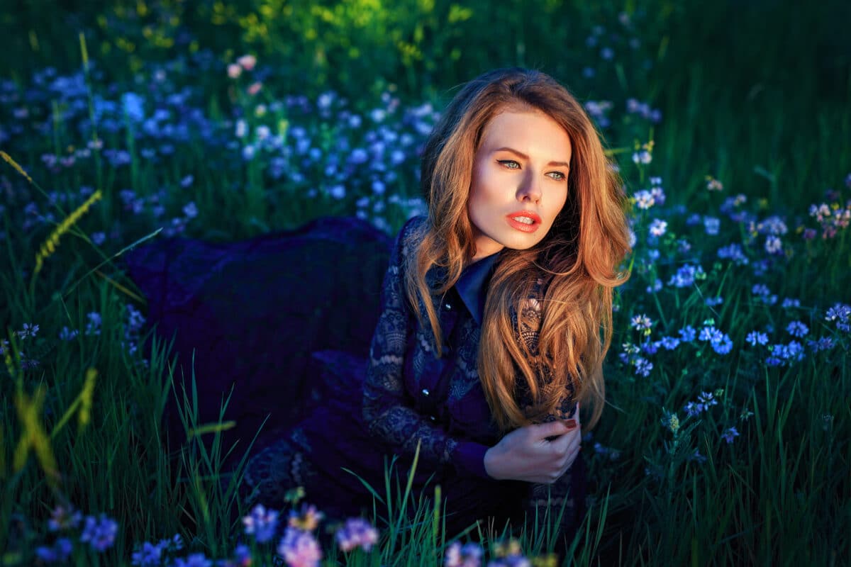 beautiful young woman in blue dress lying on grass with blue purple wild flowers