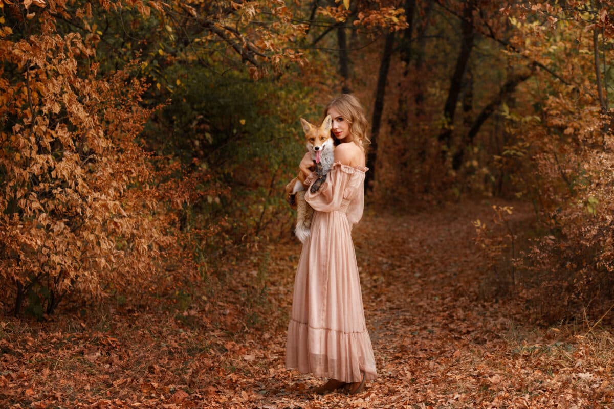 Model in a dress with a red fox in the autumn forest