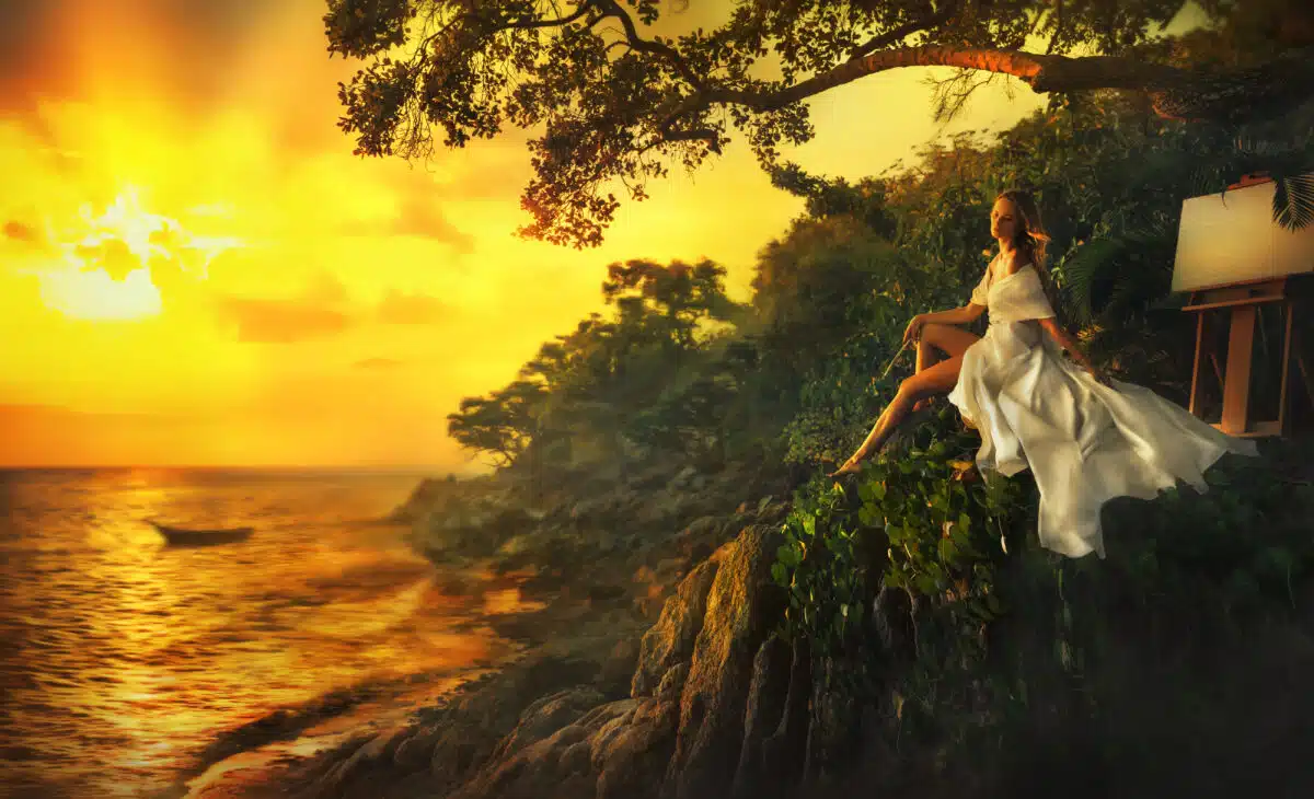 Beautiful Girl in a Long White Dress Posing near the Easel with a beautiful Nature View of the Sea during Sunset time