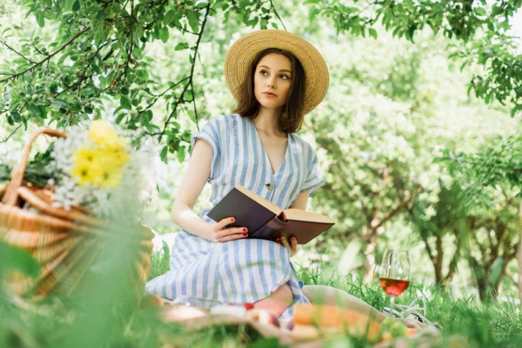 Woman in straw hat holding book having a picnic at the park.