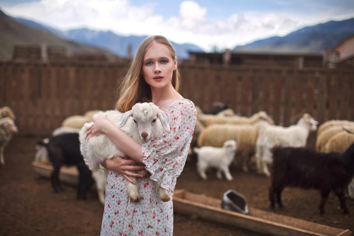 a lady holding a lamb in her arms on a farm in the mouintains